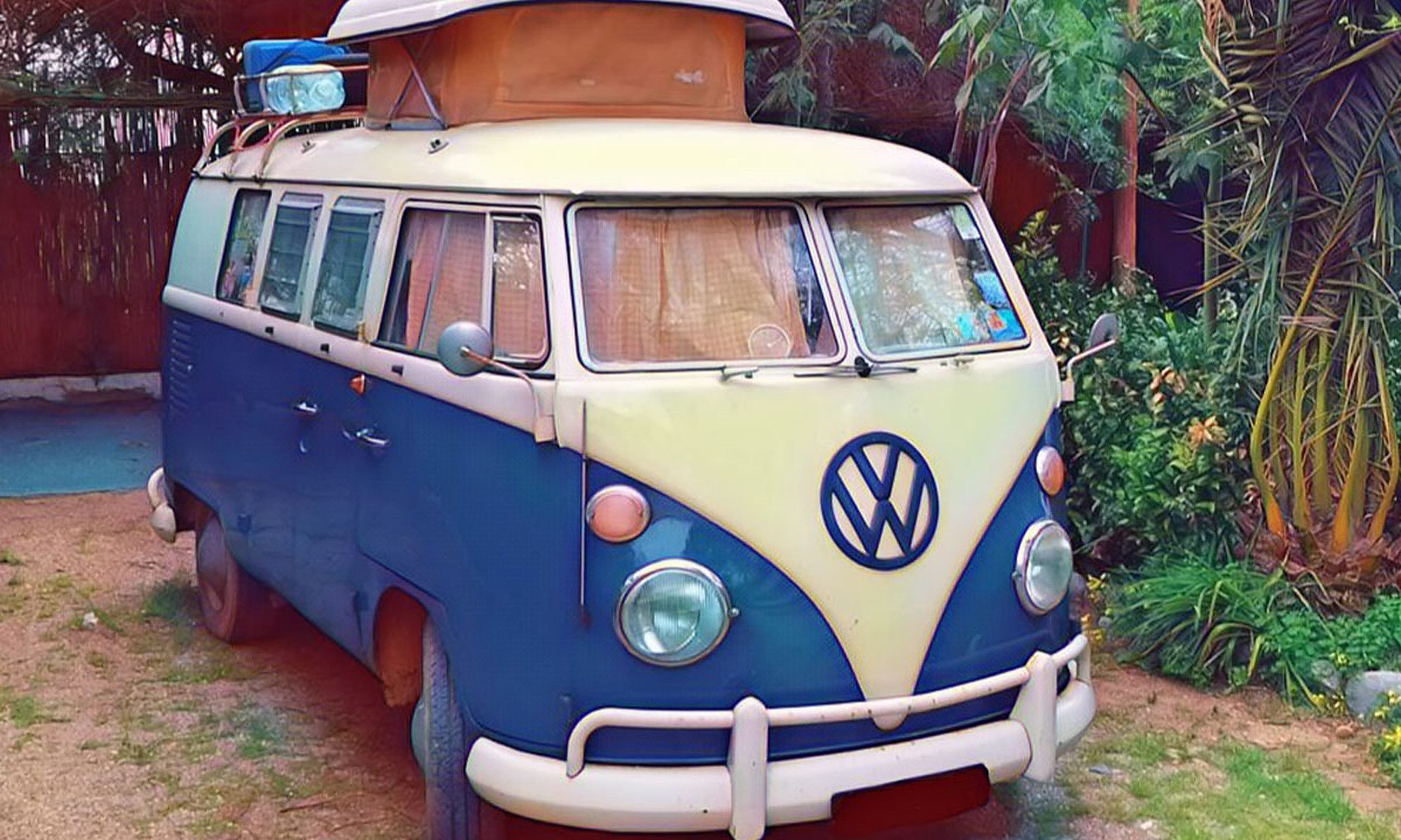 Furgoneta Volkswagen clásica azul y blanca aparcada bajo los árboles del camping